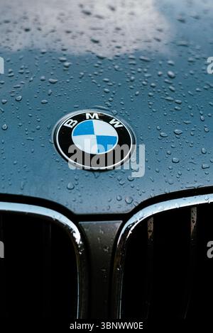 Nahaufnahme einer BMW Motorhaube mit Regentropfen auf dem Logo und einer glänzenden Oberfläche. Die Motorhaube eines SUV-Autos mit dem Emblem, das von Regentropfen bedeckt ist. sle Stockfoto