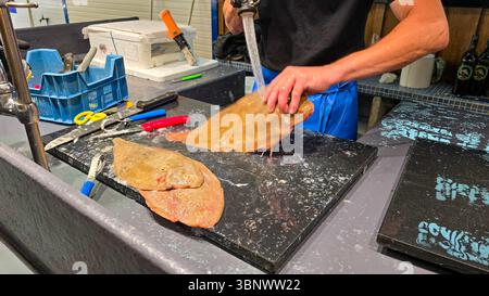 Der Fischverkäufer auf dem französischen Markt reinigt und wäscht die Seezunge vor dem Verkauf. In der Nähe befinden sich verschiedene Messer. Soulac sur Mer, Aquitaine, Frankreich. Stockfoto