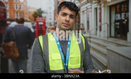 Der Mann greift das Clipboard, während er auf der Straße Notizen schreibt, während der junge hispanic-Freiwillige Lanyard und Weste trägt. Stockfoto