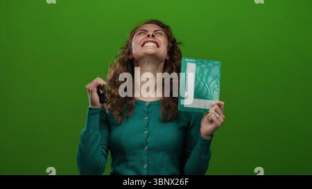 Frau, die mit Freude und Aufregung Autoschlüssel und Lernzeichen vor isoliertem grünem Hintergrund hält. Stockfoto