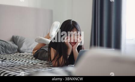 Junge Studentin, die sich im Bett entspannt, am Laptop arbeitet, online studiert Stockfoto