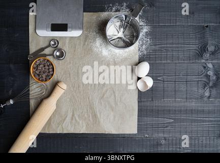 Draufsicht auf digitale Waage, Mehlsieb, Löffelset und vieles mehr auf Backpapier, bereit für hausgemachtes Backen Stockfoto