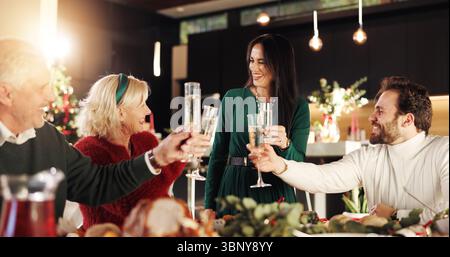 Fröhliche, große Familie und Applaus mit Sektgläsern am Esstisch zur Weihnachtsfeier. Leute, treffen und lächeln mit Alkohol oder Toast für Stockfoto