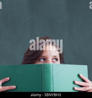 Die Frau hält ein grünes Hardcover-Buch, während sie direkt auf die dunkelgrüne Tafel in flachem Design blickt Stockfoto