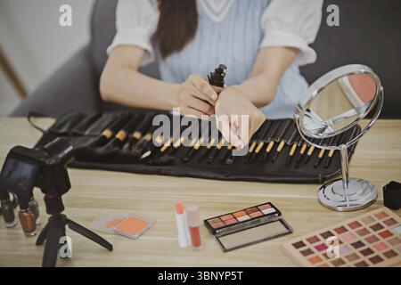 Beauty-Blogger. Fröhliche asiatische Vloggerin zeigt Kosmetikprodukte und gibt Ratschläge für ihren Beauty-Blog Stockfoto