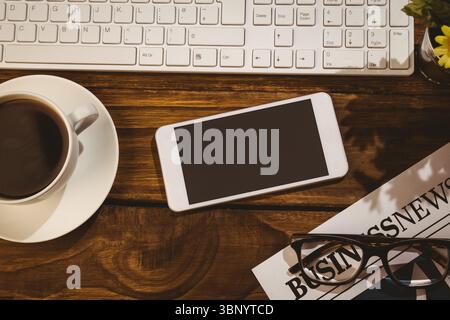 Weißes Smartphone über dem Holztisch mit Tastatur, Kaffee, Zeitung, Gläsern und Topfpflanze Stockfoto