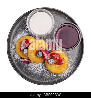 Food Stillleben, Hüttenkäsepfannkuchen mit Beeren, Puderzucker, Marmelade und Sauerrahm auf schwarzer Platte auf weißem Hintergrund Stockfoto