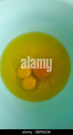In einer hellblauen Schüssel, die bereit zum Kochen ist, sehen Sie frische Eier aus nächster Nähe, und zeigen Sie ihre lebhaften Eigelbe und klaren Eiweiß für kulinarische Inspirationen und Stockfoto