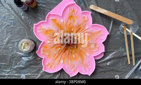 Lebendige Kunst aus Kunstharz mit Blumendesign in einer rosafarbenen Silikonform mit Werkzeugen und Farben für inspirierende künstlerische Projekte zu Hause oder in Werkstätten Stockfoto