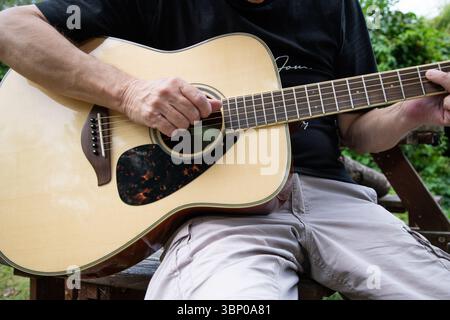 Nahaufnahme eines Mannes, der draußen eine Akustikgitarre spielt, die Details seiner Hände und seines Instruments in natürlichem Licht erfasst und Musik und Relaxatio hervorruft Stockfoto
