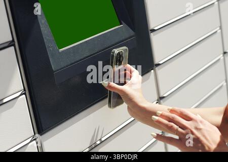 Frau scannt QR-Code auf dem Smartphone, um das Schließfach zu öffnen. Modernes Selbstbedienungspaket, Abholort. Kontaktlose Lieferung im Außenbereich. Stockfoto