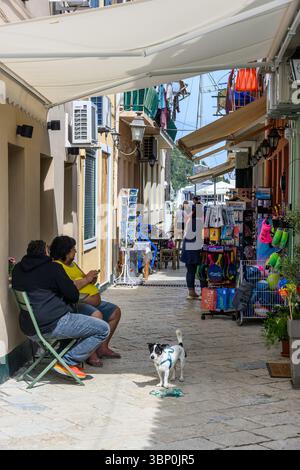 12-19/05/2025 Lakka, Paxos, Griechenland. Die Einheimischen genießen einen Kaffee im Schatten einer Markise in einer Fußgängerzone mit Souvenirläden. Foto © Simon Grosset Stockfoto