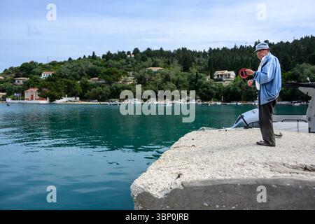12-19/05/2025 Lakka, Paxos, Griechenland. Älterer Mann, der nur mit einer Schlange im Hafen angelt. Foto © Simon Grosset Stockfoto