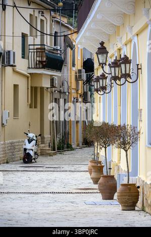 12-19/05/2025 Lakka, Paxos, Griechenland. Straßenszene mit cremefarbenen Wänden, blauen Bogenfenstern, Roller und Topfpflanzen. Foto © Simon Grosset Stockfoto