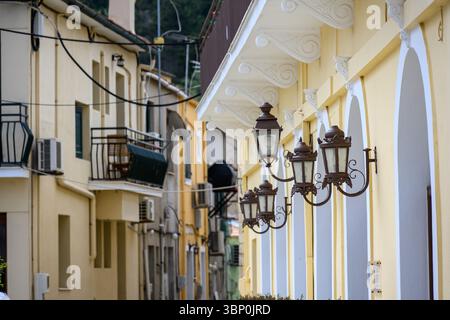 12-19/05/2025 Lakka, Paxos, Griechenland. Straßenszene mit cremefarbenen Wänden, blauen Bogenfenstern, Lampen und Topfpflanzen. Foto © Simon Grosset Stockfoto