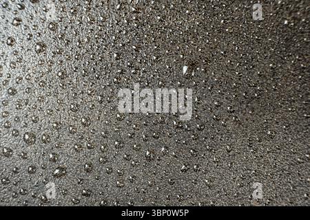 Wassertropfen auf einer gusseisernen Makrooberfläche. Gusseiserne Kochgeschirr Pflege, rostbeständig, abstraktes Muster. Stockfoto