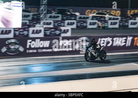 Motion Blur Drag Racing bei Nacht, bei dem Motorräder auf der Rennstrecke mit Zuschauern in der Nähe antreten Stockfoto