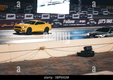 Motion Blur Drag Racing bei Nacht, bei dem Autos auf der Rennstrecke mit Zuschauern in der Nähe konkurrieren Stockfoto