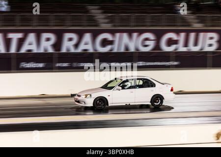 Motion Blur Drag Racing bei Nacht, bei dem Autos auf der Rennstrecke mit Zuschauern in der Nähe konkurrieren Stockfoto