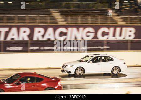 Motion Blur Drag Racing bei Nacht, bei dem Autos auf der Rennstrecke mit Zuschauern in der Nähe konkurrieren Stockfoto