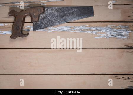 Handsäge mit Holzgriff oben links auf abgenutztem beigefarbenen Holztisch. Der Rest des Rahmens lässt viel Platz für Text oder Design. Stockfoto