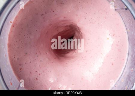 Der Prozess der Herstellung eines Erdbeeren-Milchshakes, bei dem alle Zutaten in einem Mixer geschüttet werden Stockfoto