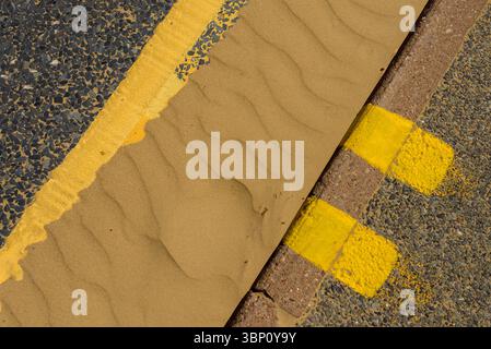 Gelbe Bordsteinmarkierungen, doppelte gelbe Linien und Sand in der Dachrinne Stockfoto
