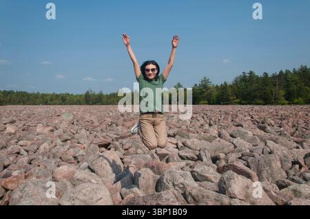 Eine chinesin, die an einem sonnigen Sommertag im Hickory Run Boulderfeld in Lake Harmony pennsylvania vor Freude hüpft. Stockfoto