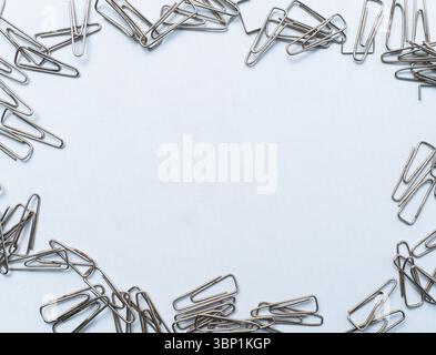 Ästhetische Anordnung silberner Büroklammern, die eine Grenze auf einer weißen Oberfläche bilden. Stockfoto