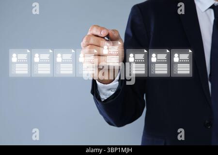 Personalmanager überprüft den Lebenslauf des Kandidaten auf einem virtuellen Bildschirm vor grauem Hintergrund, Nahaufnahme Stockfoto
