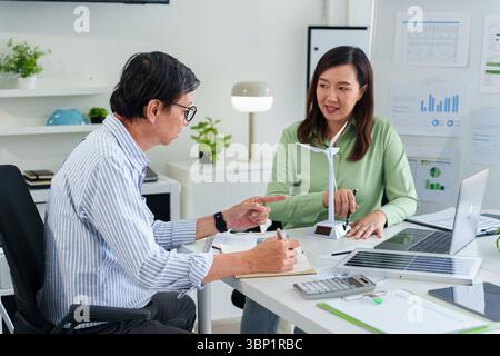Erwachsene asiatische Geschäftsleute arbeiten gemeinsam an nachhaltigen Strategien mit Schwerpunkt auf Modellen für saubere Energie in einer modernen Büroumgebung. Stockfoto