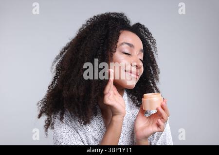 Schöne brasilianische Frau mit einem Glas Kollagencreme auf grauem Hintergrund Stockfoto