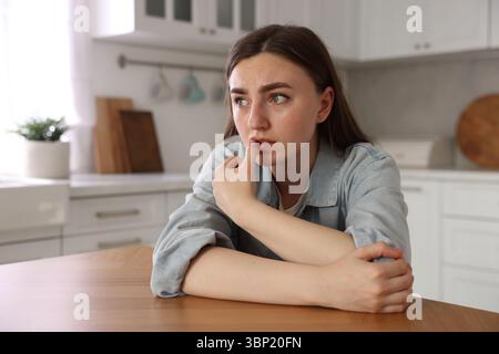 Verängstigte Frau, die an Paranoia leidet, am Tisch in der Küche Stockfoto