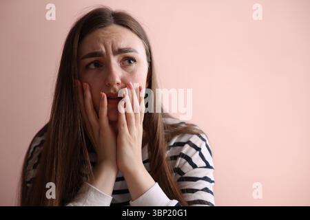 Verängstigte Frau, die an Paranoia leidet, in der Nähe einer beigefarbenen Wand drinnen, Platz für Text Stockfoto