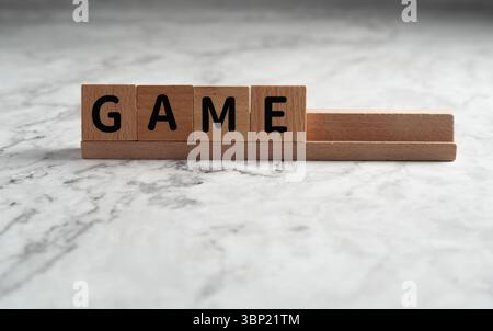 Das Wort „SPIEL“ wurde mit hölzernen Buchstabenblöcken formuliert, die auf einem Holzgestell aufgestellt waren, isoliert vor einem hellen, strukturierten Hintergrund Stockfoto