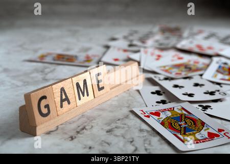 Auf einem Holzgestell befinden sich Briefblöcke mit der Schreibweise „SPIEL“, auf denen Spielkarten auf einer strukturierten Oberfläche verteilt sind Stockfoto