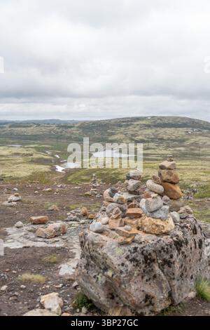 Mehrere steinhügel sind sorgfältig ausgeglichen auf einem felsigen Tundra-Plateau mit Blick auf moosige Hügel, Seen und verschneite Flecken in der Nähe von Teriberka, Russland Stockfoto