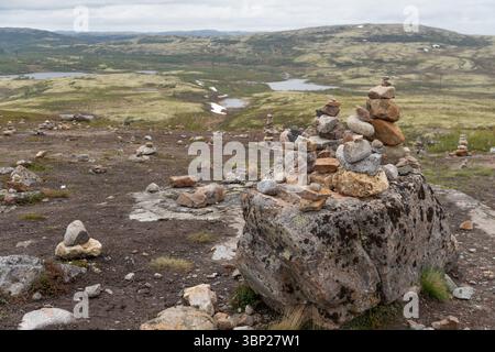 Mehrere steinhügel sind sorgfältig ausgeglichen auf einem felsigen Tundra-Plateau mit Blick auf moosige Hügel, Seen und verschneite Flecken in der Nähe von Teriberka, Russland Stockfoto