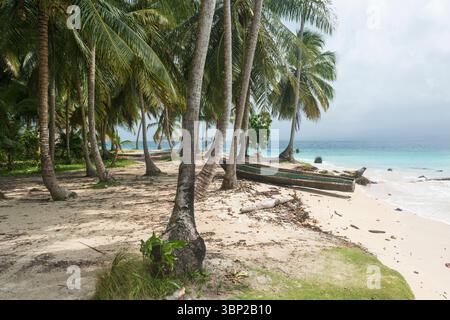 Kleines Holzboot am Strand zwischen Palmen, Insel in der Ferne. San Blas Archipel, Panama. Stockfoto