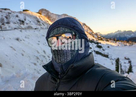 Ein Mann mit schwarzer Jacke und Schal steht im Schnee. Er trägt eine Sonnenbrille und einen Hut Stockfoto