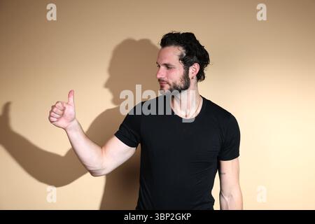 Ein bärtiger Mann in einem schwarzen T-Shirt schaut nach rechts, während er eine Geste nach oben zeigt, die Zustimmung oder eine positive Einstellung zu etwas zeigt Stockfoto