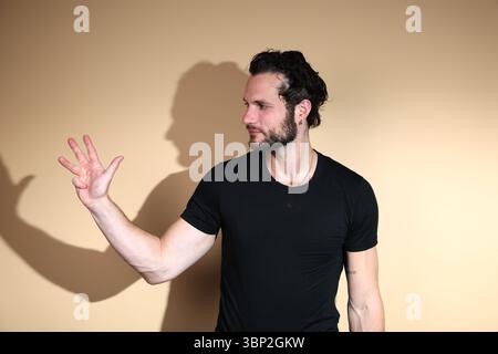 Nach rechts blickt ein bärtiger Mann in einem schwarzen T-Shirt vier Finger hoch, wahrscheinlich zählt er, zeigt die Zahl vier oder zeigt eine vierte Stockfoto