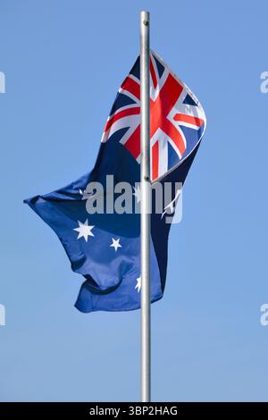 Die Nationalflagge Australiens fliegt stolz an einem wunderschönen Sommertag mit blauem Himmel auf einem Fahnenmast. Stockfoto