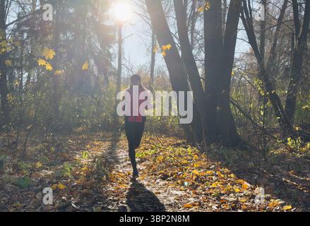 Waldweg im Herbst. Herbstläuferin, die in wunderschönen Laubwäldern läuft, Natur Hintergrund. Asiatische glückliche Sportfrau, die im Freien trainiert. Stockfoto