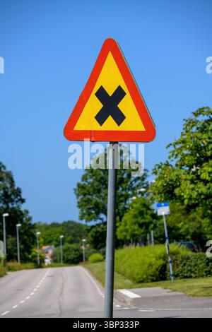 In einer städtischen Umgebung wird ein dreieckiges Warnschild angezeigt, das die Fahrer auf bevorstehende Kreuzungen aufmerksam macht. Die leuchtenden Farben heben aga hervor Stockfoto