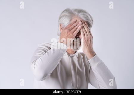 Ein älterer Mann mit Kapuze hält die Hände vor das Gesicht Stockfoto