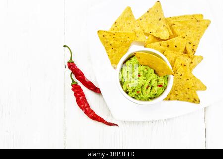 Guacamolensauce in einer Schüssel mit Maischips auf Teller, heiße Pfefferschoten auf Holzbrett Hintergrund von oben Stockfoto