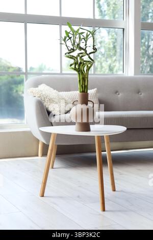 Vase mit grünen Bambusstielen auf dem Tisch in der Nähe des Fensters Stockfoto