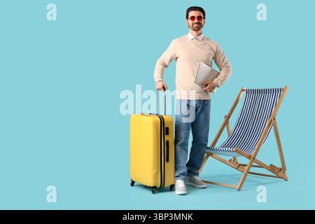 Junger Geschäftsmann mit Laptop und Koffer in der Nähe des Liegestuhls auf blauem Hintergrund. Sommerferienkonzept Stockfoto
