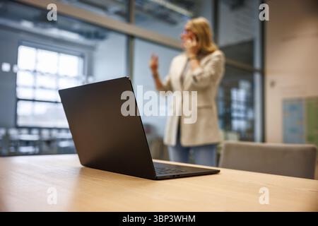 Führungsrolle im Unternehmensgeschäft. Laptop auf dem Schreibtisch. Frau, die während eines Online-Meetings in modernen Büroräumen mit dem Mobiltelefon spricht Stockfoto
